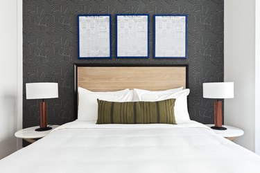 Modern bedroom with light wood headboard, matching nightstands and lamps, black and white wallpaper, art.
